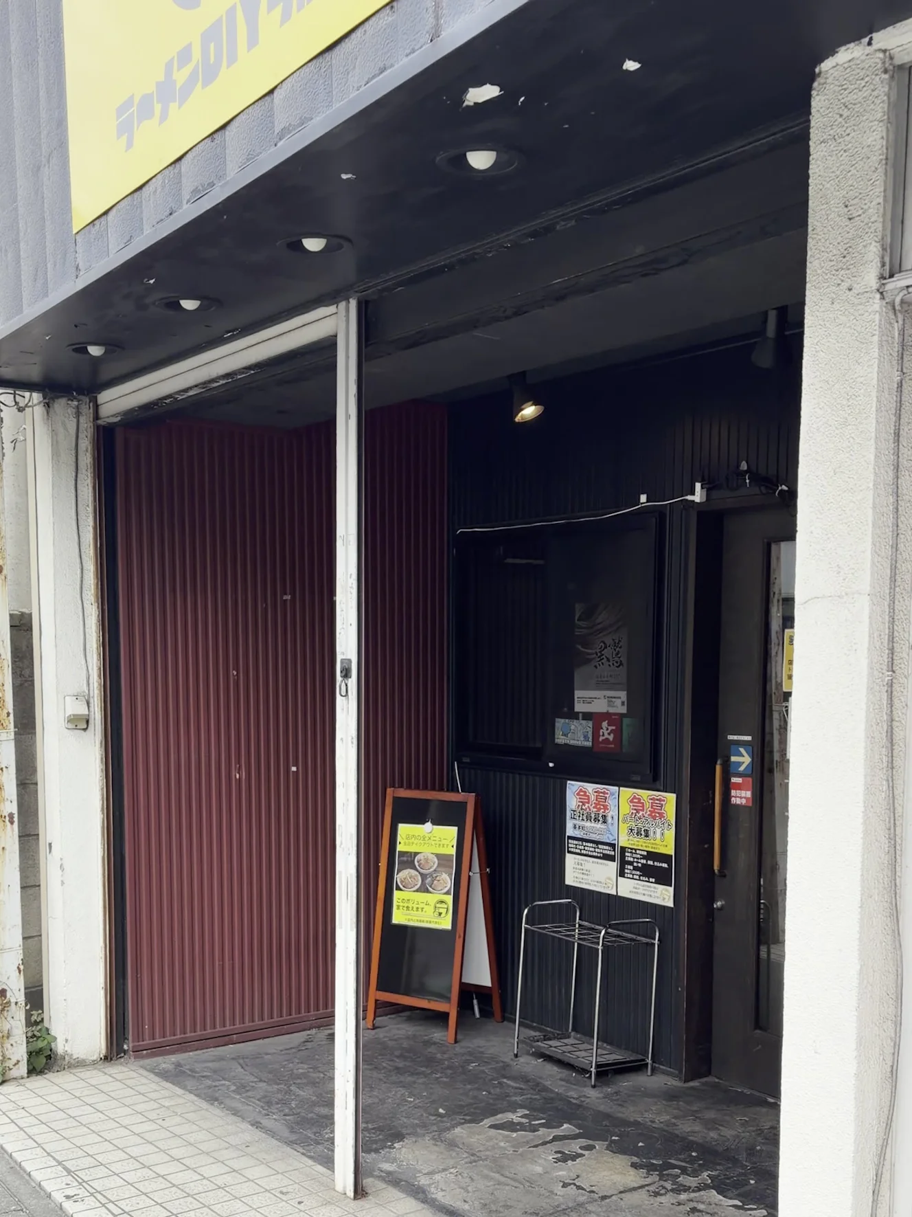 ラーメンDIYラボの外観。黄色い看板の下に入口があり、メニューの立て看板が出ている