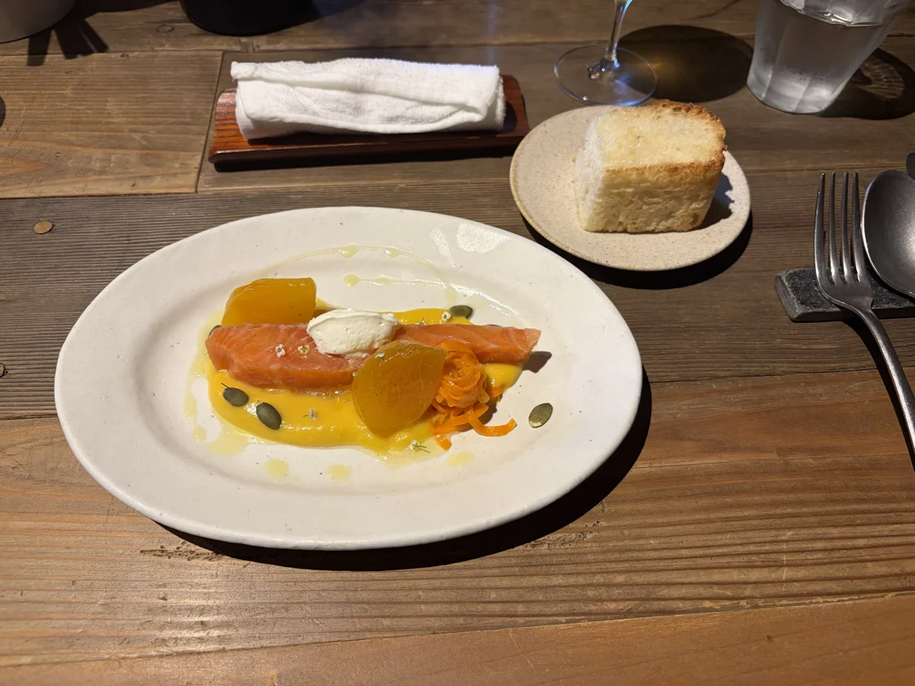 サーモンと柿のマリネ。かぼちゃのソースとクリームチーズ、かぼちゃの種が添えられ、横に焼き立てのフォカッチャ