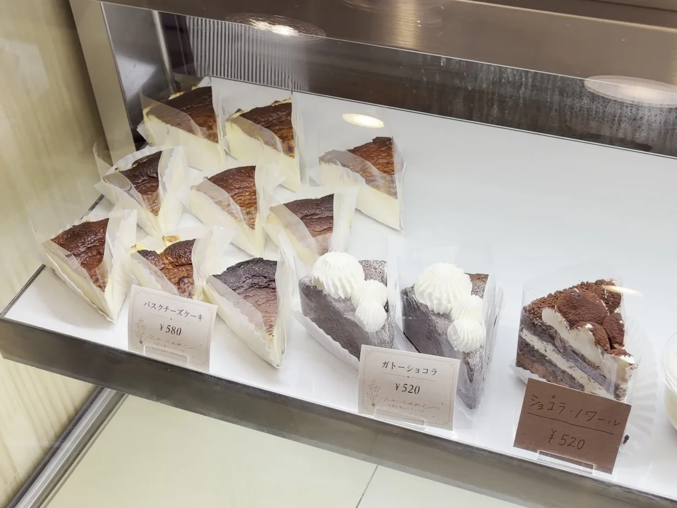 ショーケースの棚に並ぶ、表面を焦がしたバスクチーズケーキ。手前にバスクチーズケーキ ¥580の札