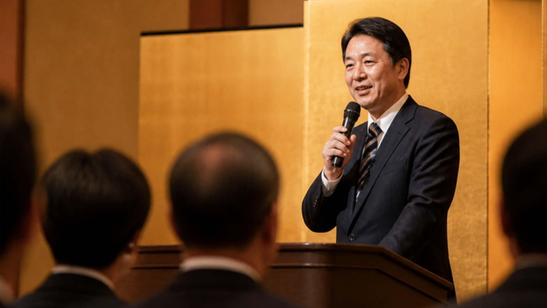 納会でマイクを持ち挨拶する役員