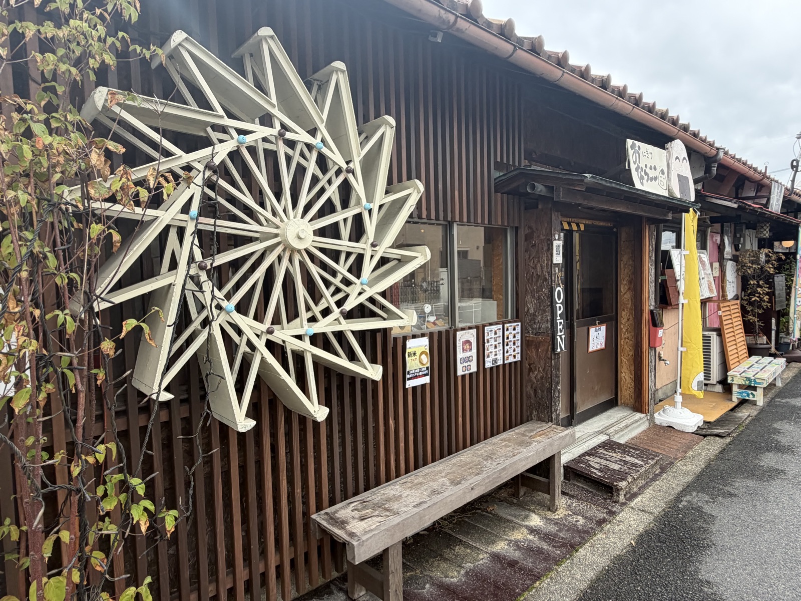 おにぎり店「ならここ」の外観。板張りの壁に白い大きな水車が取り付けられ、入口に縦書きの「OPEN」札と黄色い日よけ