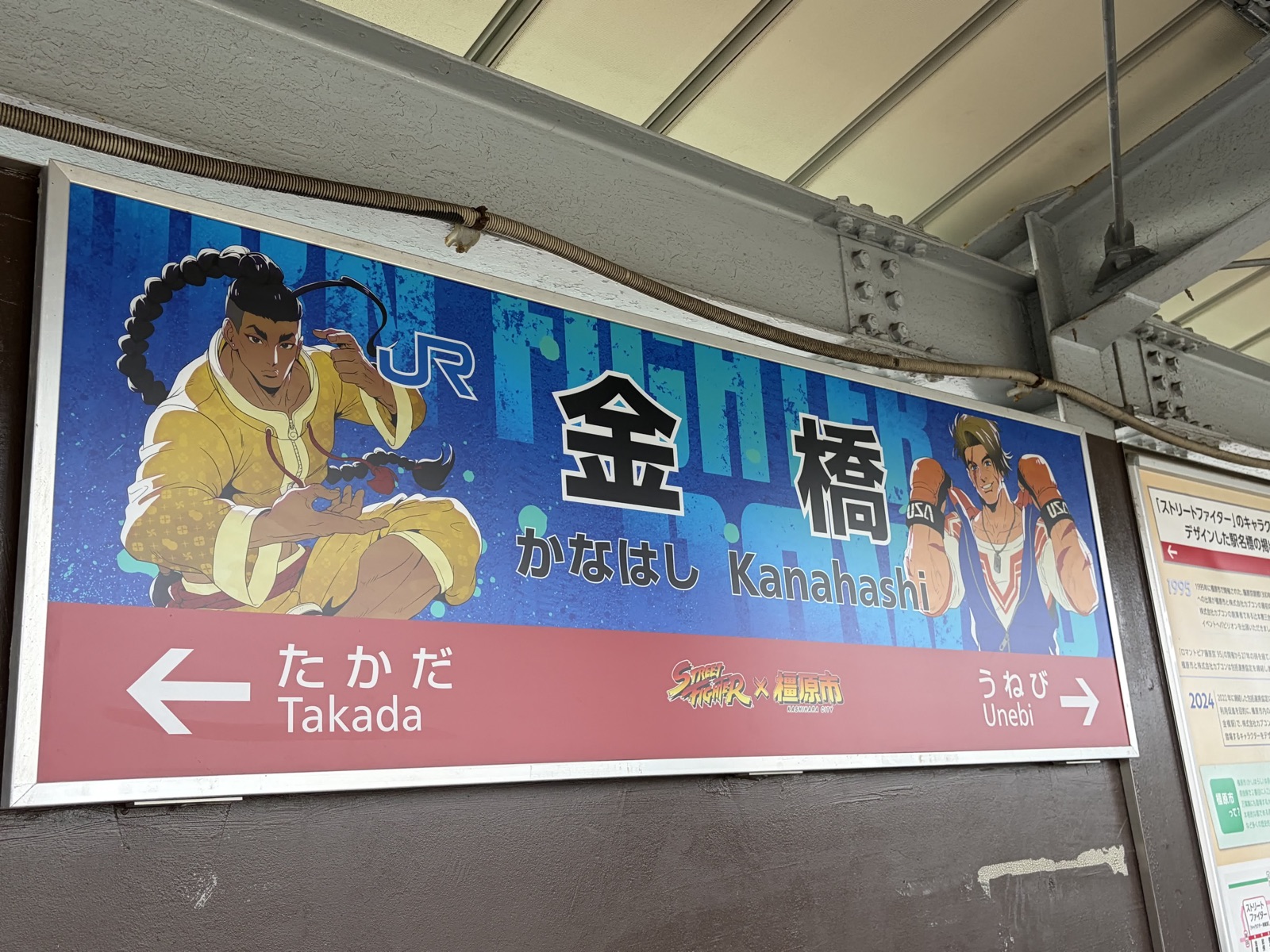 JR金橋駅の駅名標。青地に「金橋 かなはし Kanahashi」、左右にストリートファイターのキャラクターが描かれている
