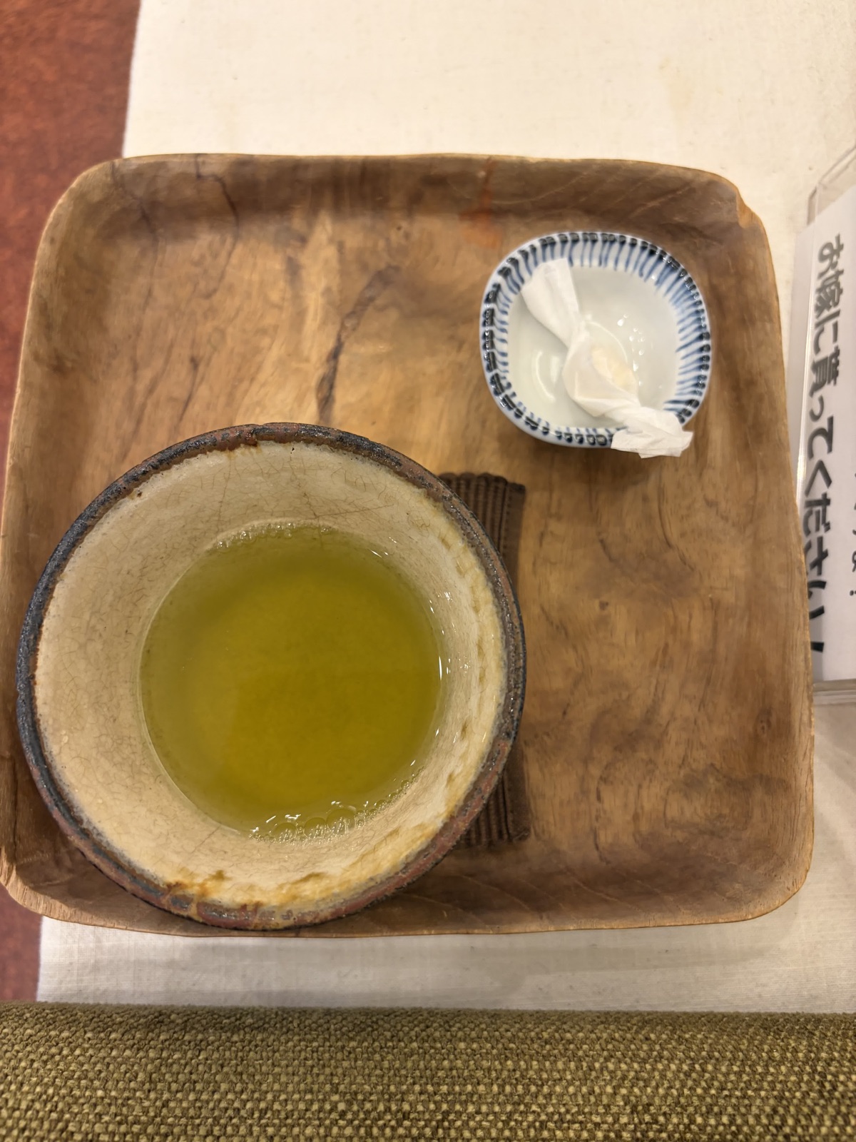 木を削り出した角盆に、黄緑色のお茶が入った湯呑と、藍色の縁の小皿に置かれたおしぼり