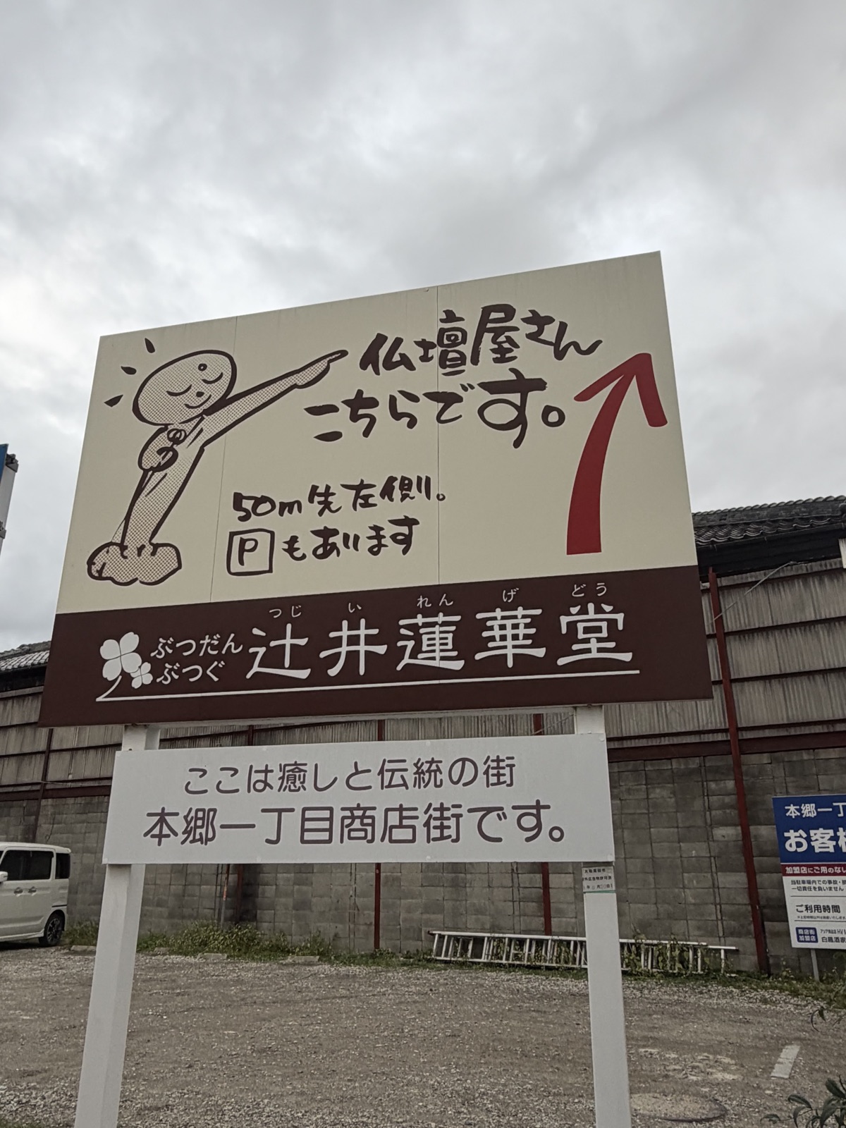 「仏壇屋さん こちらです。50m先左側。Pもあります」と書かれた大きな立て看板。下に「辻井蓮華堂」、手前に商店街の案内板