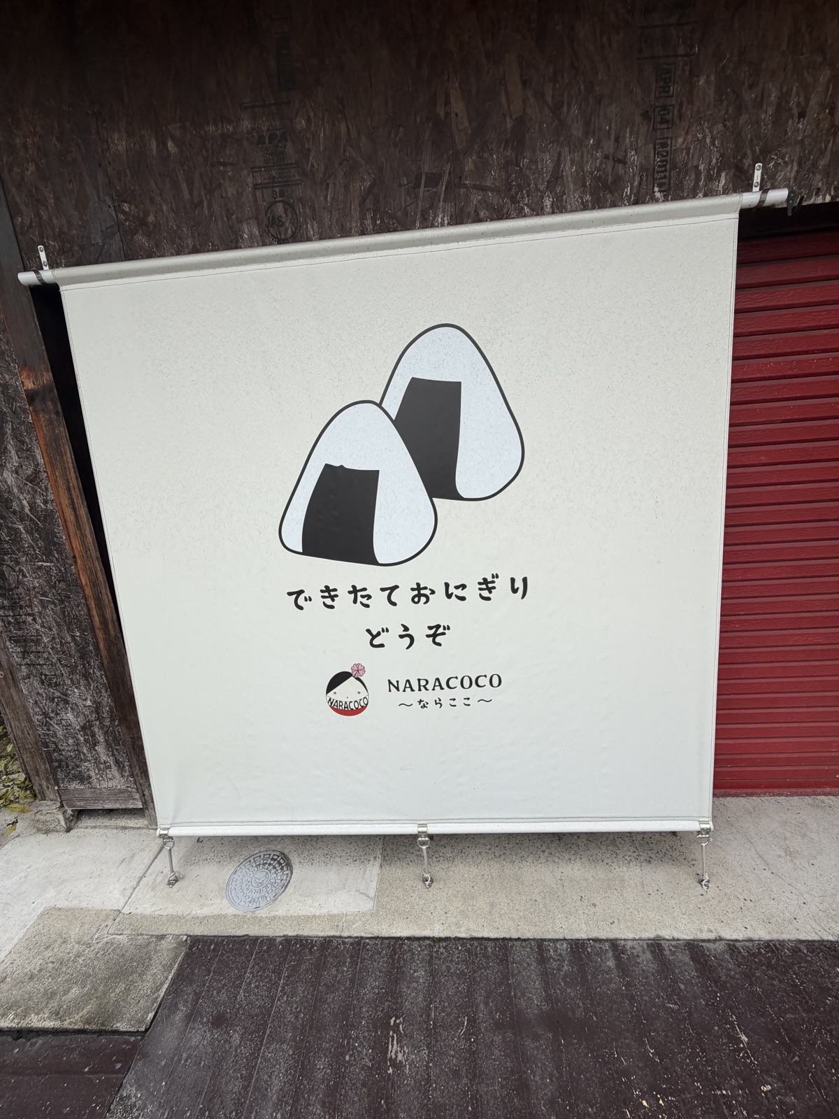 白い日よけ幕に描かれた大きなおにぎり2つのイラスト。下に「できたておにぎり どうぞ」「NARACOCO 〜ならここ〜」