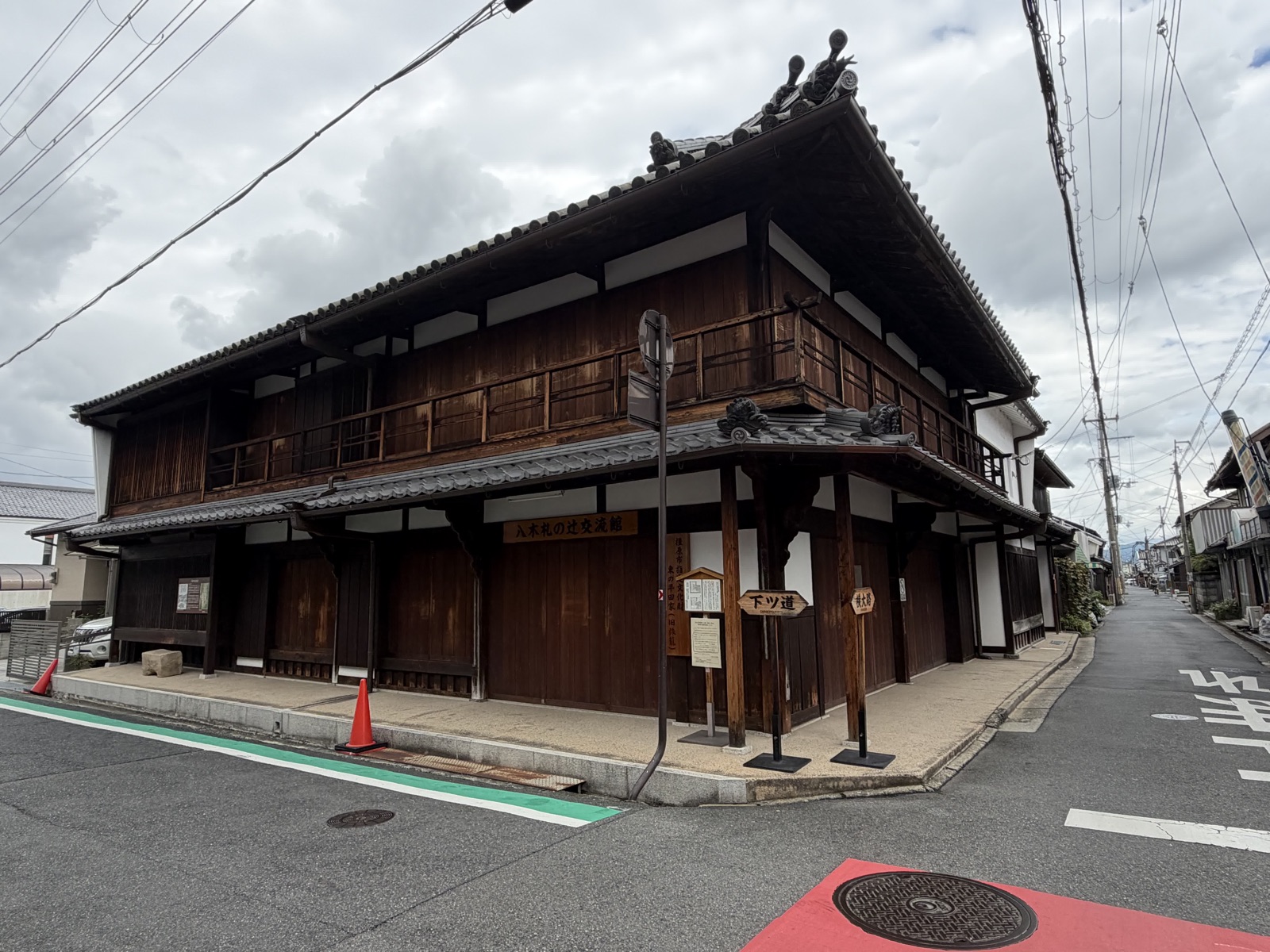 八木札の辻交流館の外観。二階建ての木造町家に館名の看板が掛かり、角に「下ツ道」「横大路」の木の道標が立つ