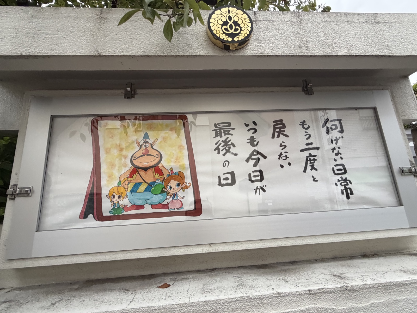 ガラスケースに入った手描きの掲示。「何げない日常 もう二度と戻らない いつも今日が最後の日」の筆文字と、鬼と妖精の色鉛筆画