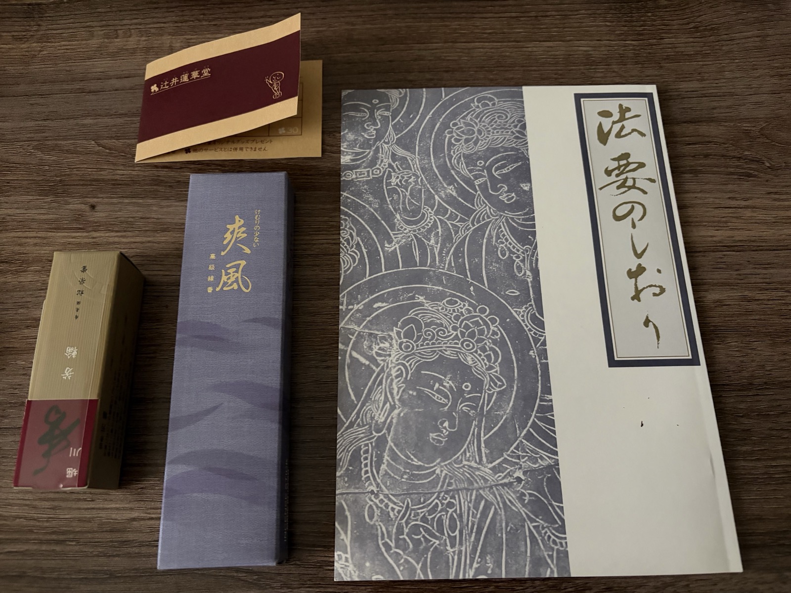 木目のテーブルに並べた、紫の箱に入った高級線香「爽風」、細長い箱のお線香、辻井蓮華堂のカード、仏画が刷られた表紙の冊子「法要のしおり」