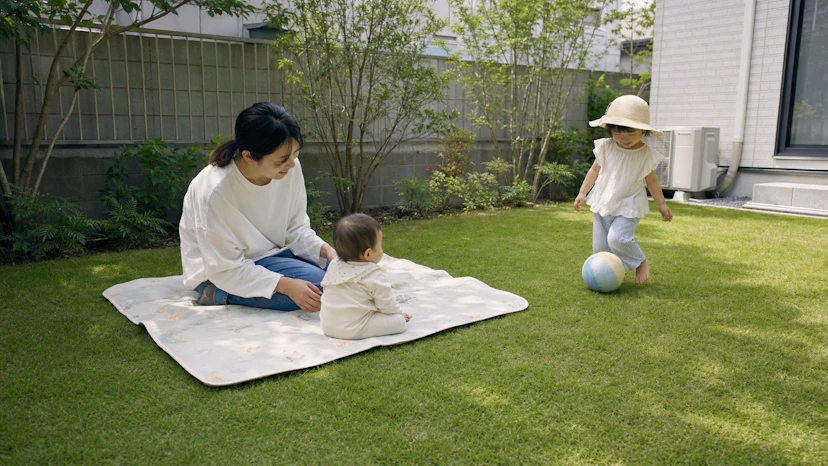 木陰の芝生で保護者に見守られながら遊ぶ赤ちゃんと子ども